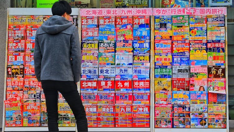 Photo by Bagus Pangestu - Japanese man Standing Wearing Gray Hoodie in Front of Magazine in Rack
